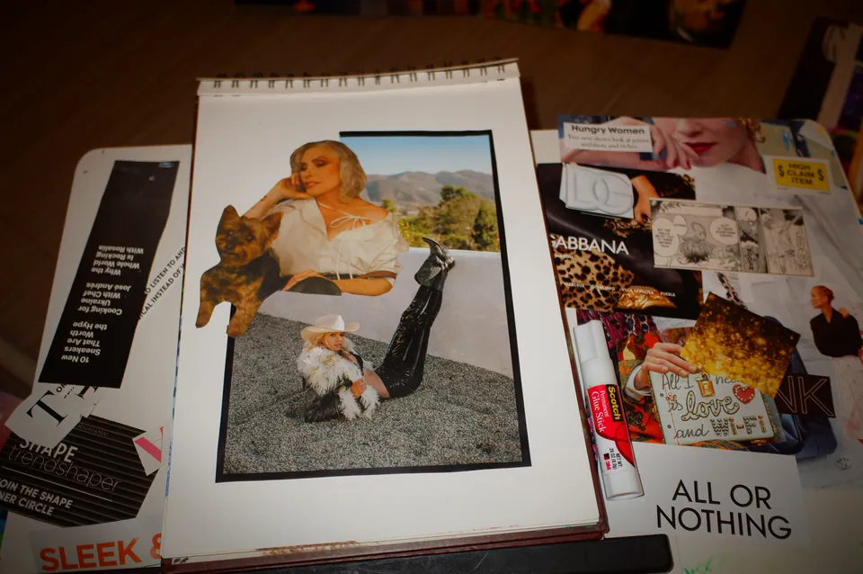 A collage in progress on a spiral sketchbook: a woman in white on a rooftop with a small dog, a figure in a fur coat and cowboy hat below, magazine pages spread around it.