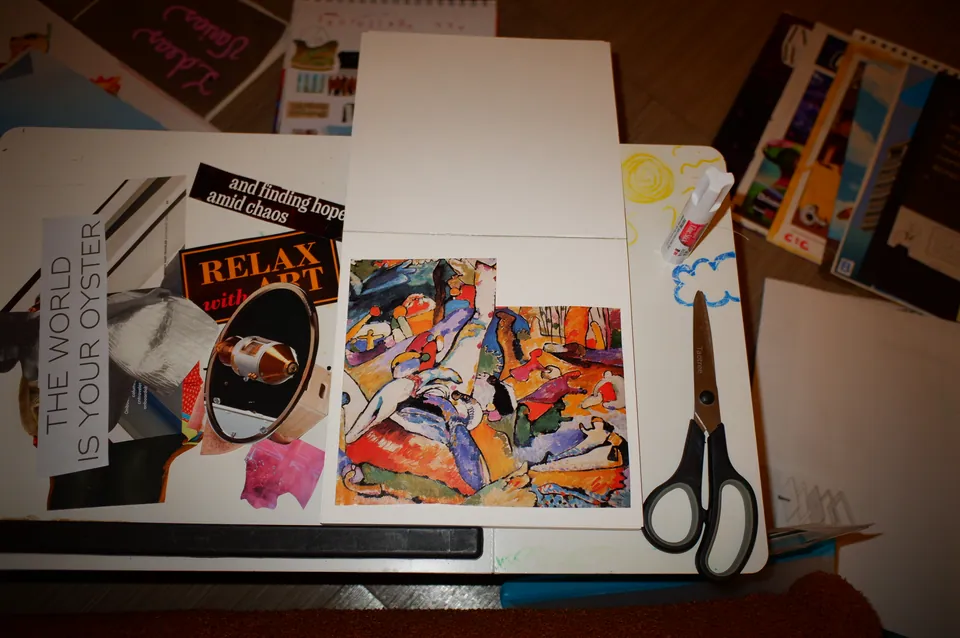 An open sketchbook with a bright abstract collage panel and cut-out words, The world is your oyster and Relax with art, beside black scissors and a glue stick.