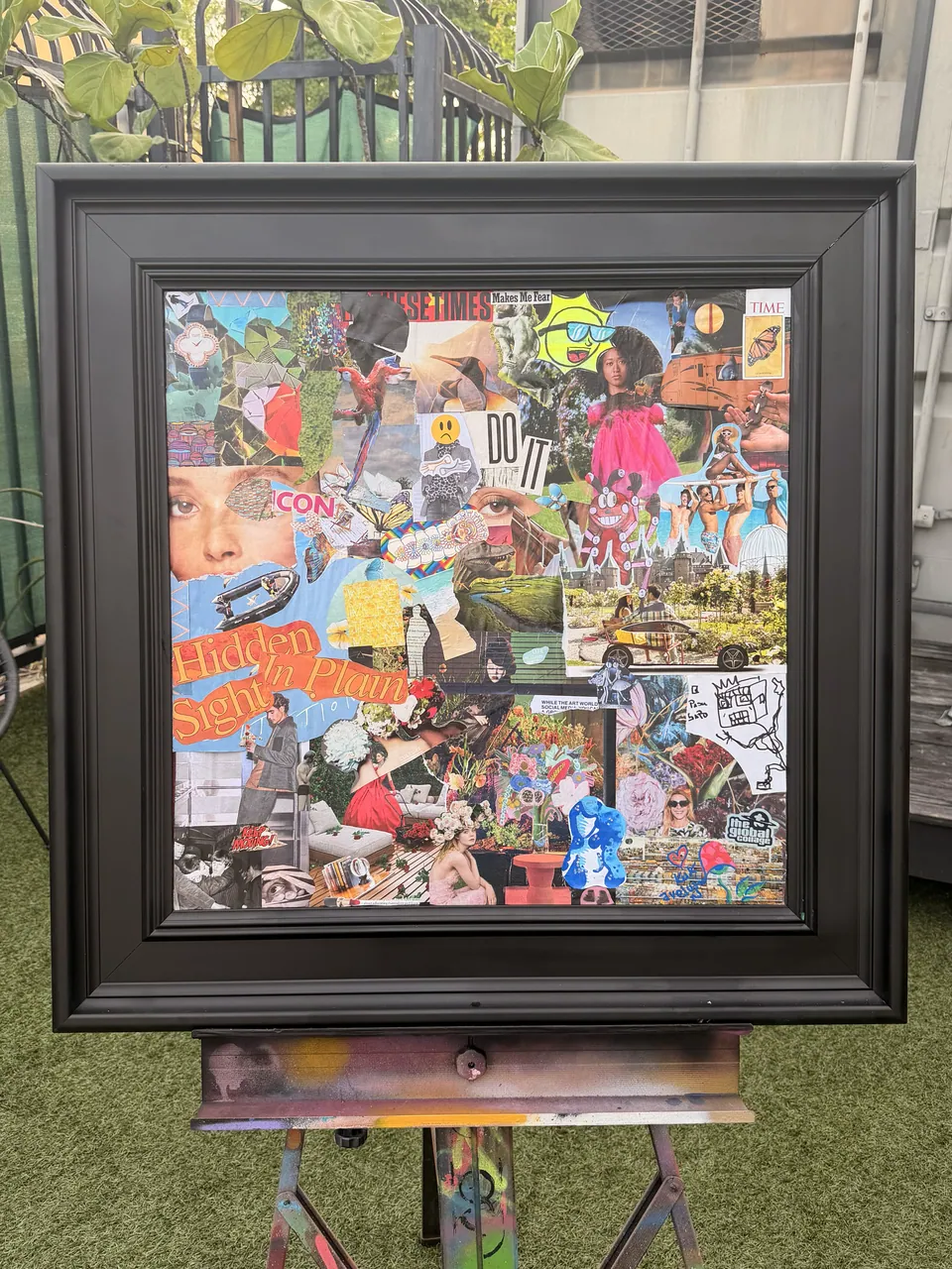 The Local Collage #3: The Butterfly Effect, collage on canvas in a deep black frame on a paint-splashed easel, outdoors on green turf.